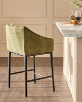 Julep bar stool in olive green fabric with black metal legs, shown at a marble-top counter in a neutral interior setting.
