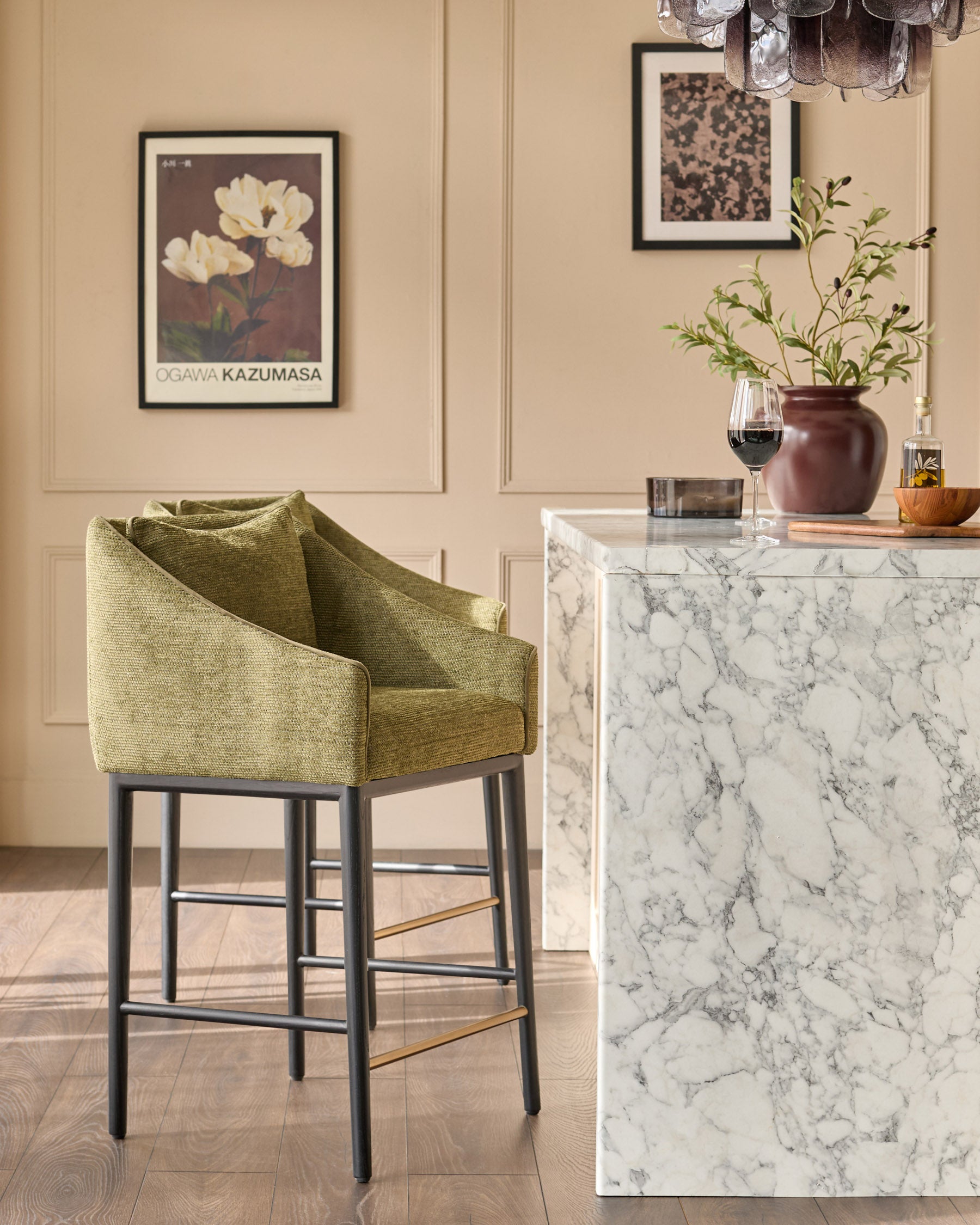 Olive-green upholstered bar stool with black wooden legs and brass footrests, shown in a styled interior setting.