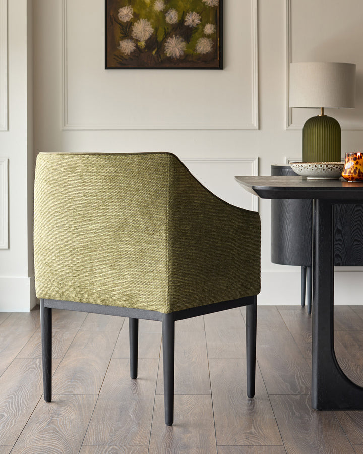 Julep dining chair in olive green fabric with curved backrest and dark wooden legs, shown in a styled interior setting.