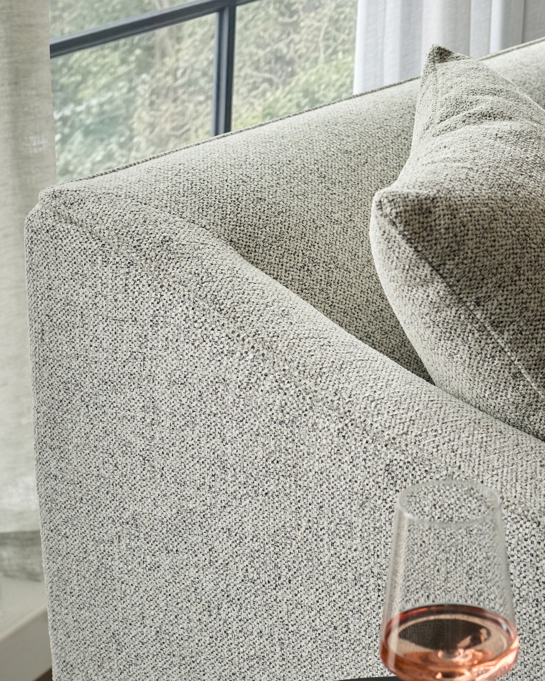 Julep Blackwood 2-seater sofa in grey fabric, close-up detail showing textured weave and curved armrest by window.