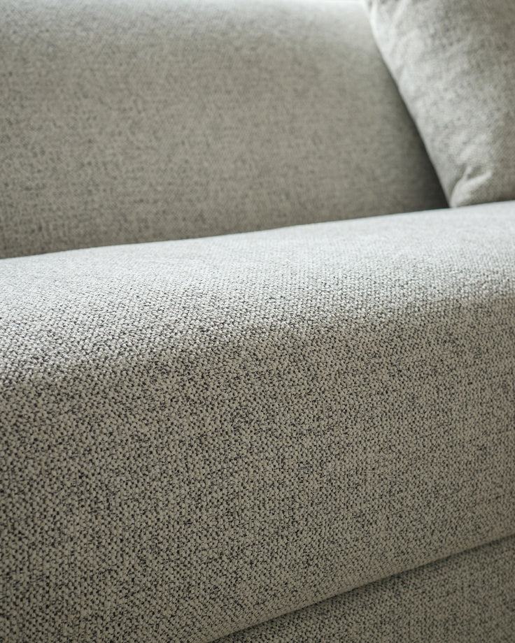 Close-up of grey fabric texture on Julep Blackwood 3-seater sofa, showing woven upholstery detail and cushioned armrest.