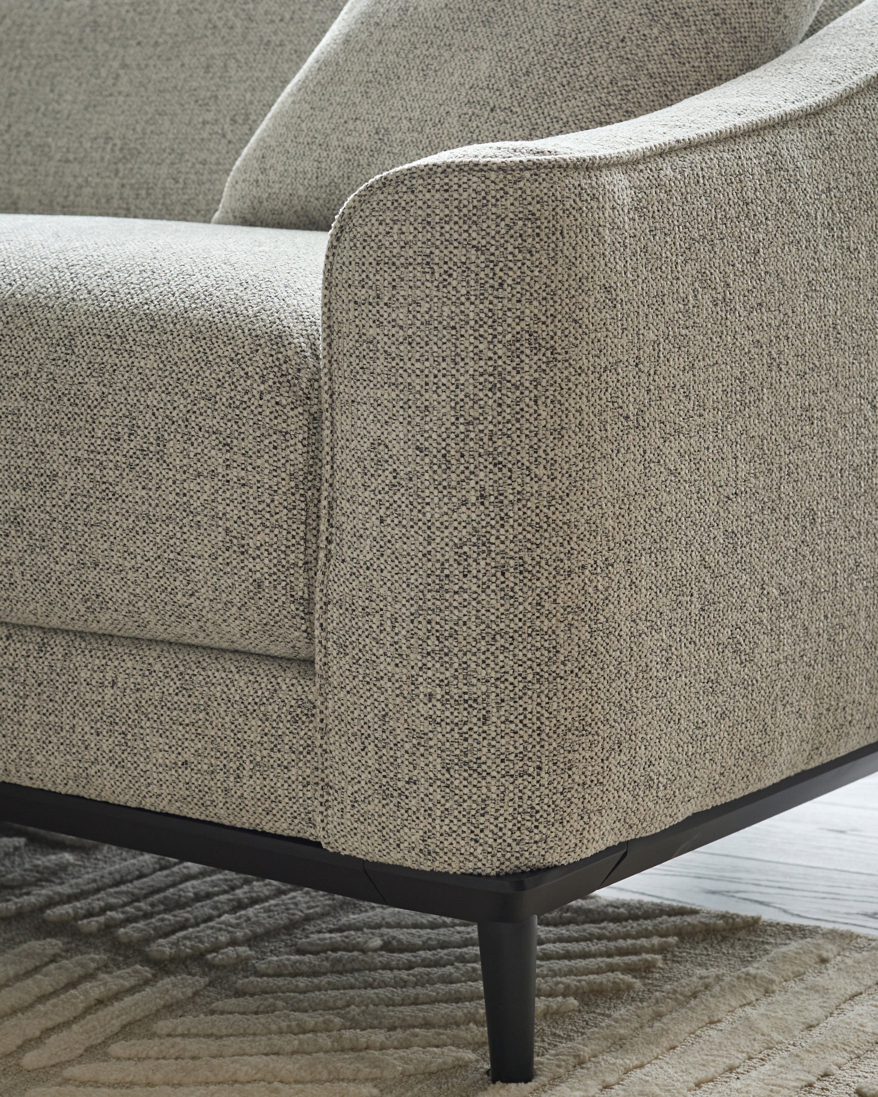 Grey fabric 2-seater sofa with curved armrests and black wooden legs, shown at close-up side angle.