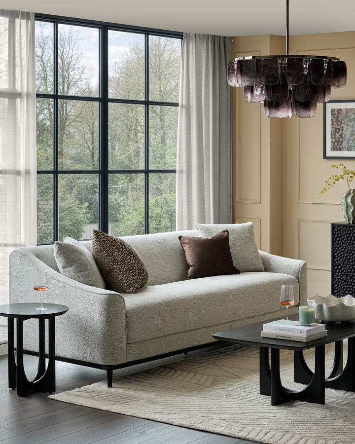 Grey fabric three-seater sofa with curved arms and black wooden legs, styled in a modern living room setting with accent pillows.