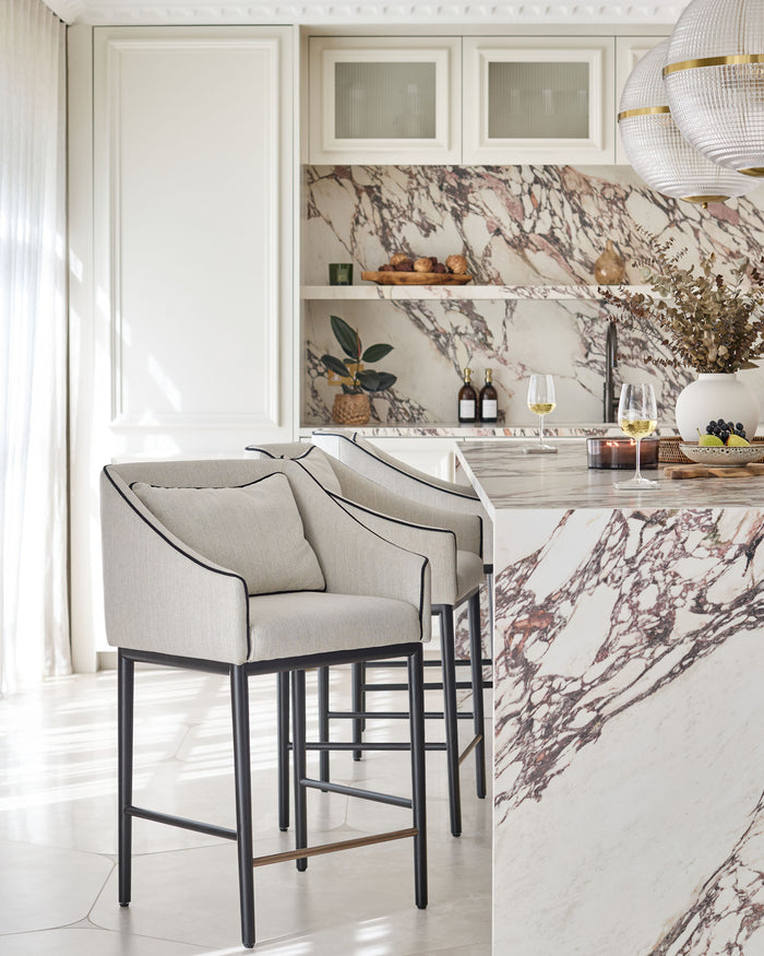 Two stylish bar stools with black legs and linen seats sit in front of a marble countertop.