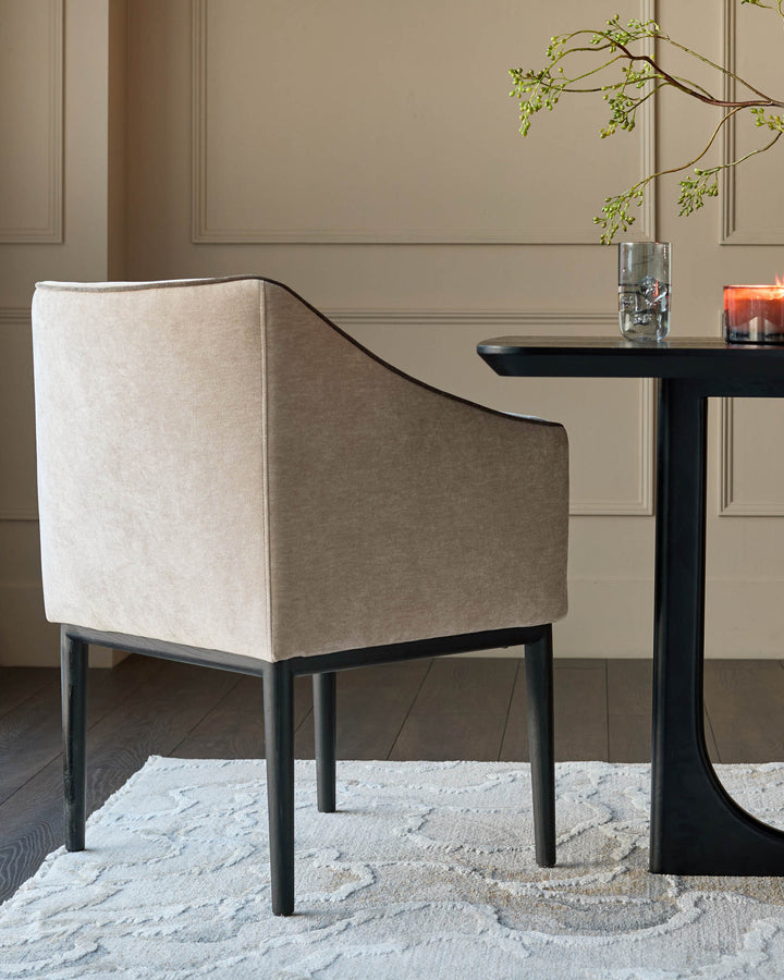 Julep dining chair in champagne fabric, featuring curved back and black wooden legs, styled at black pedestal table.
