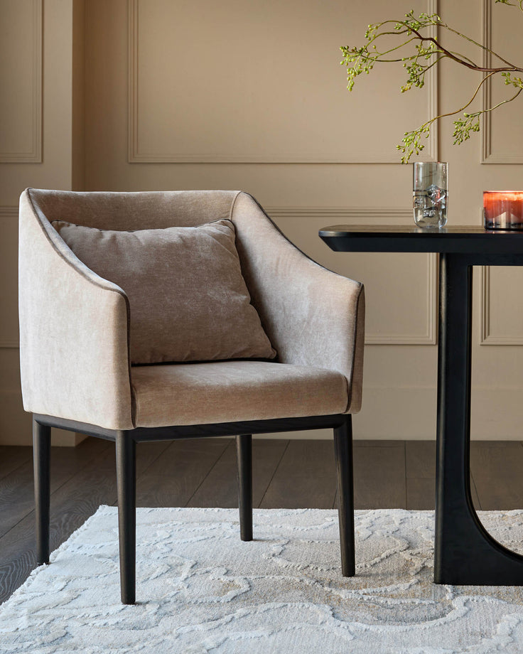 Champagne fabric dining chair with curved arms, black wooden legs, and a matching throw pillow, styled in a modern room setting.