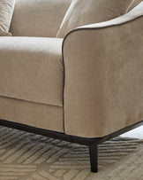 Julep Blackwood 2-seater sofa in champagne fabric, showing curved armrest and black wooden legs on patterned rug.