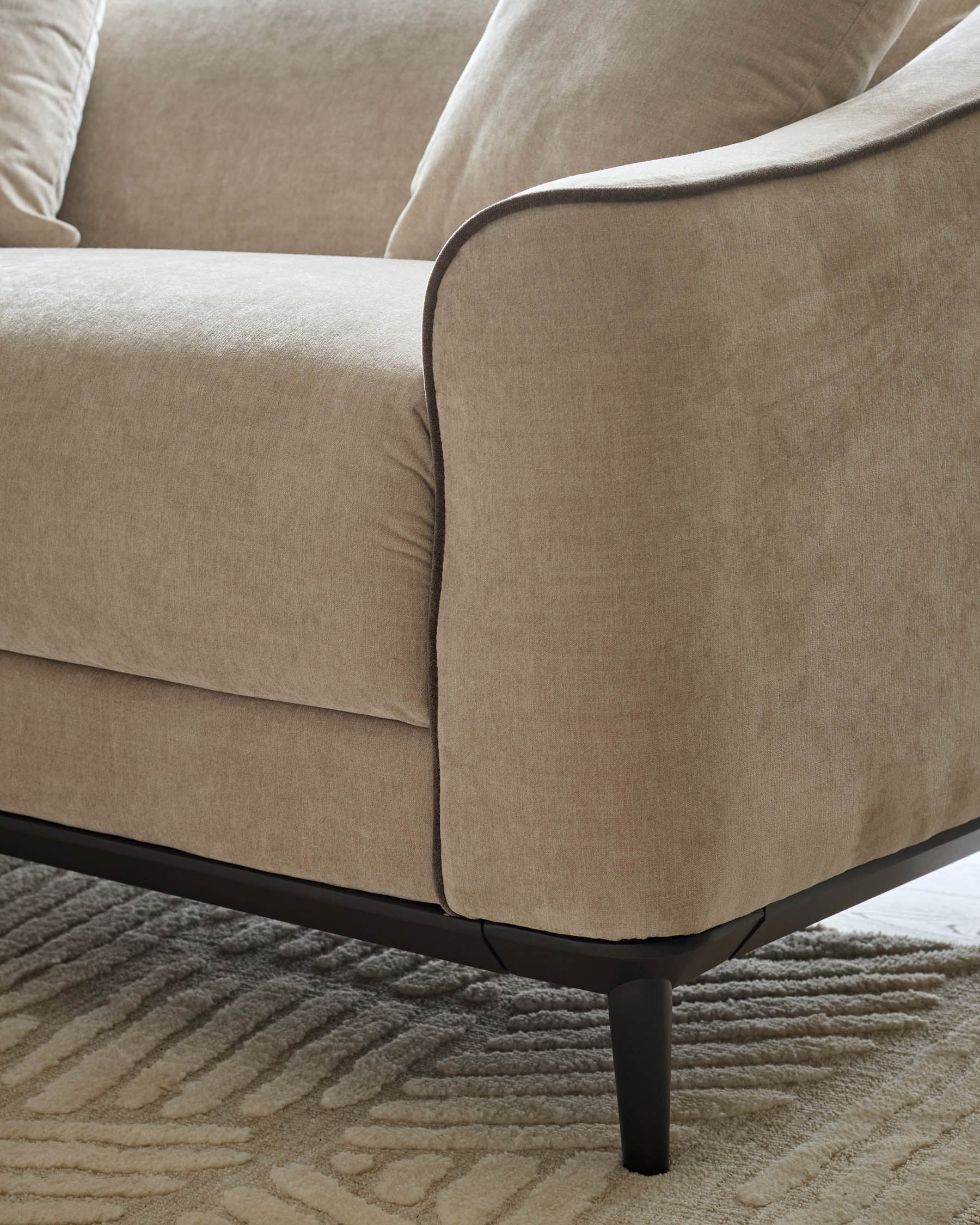 Julep Blackwood 2-seater sofa in champagne fabric, showing curved armrest and black wooden legs on patterned rug.