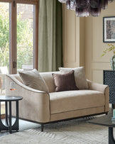 Julep Blackwood 2-seater sofa in champagne fabric with rolled arms, black legs, styled with pillows in a bright living room.