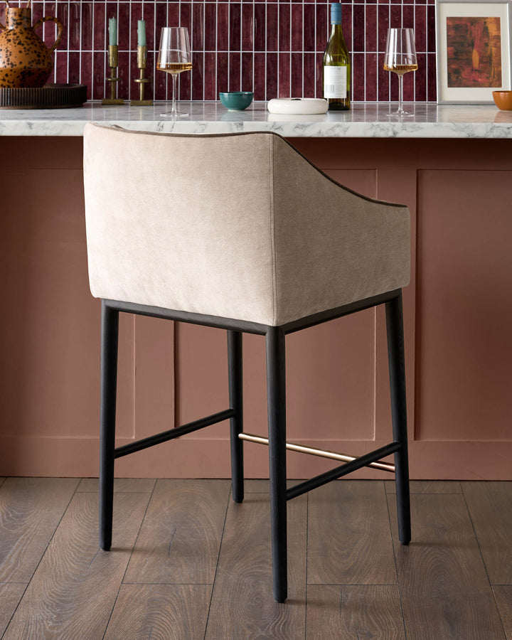 Julep bar stool in champagne fabric with black wooden legs and footrest, shown at a bar counter.