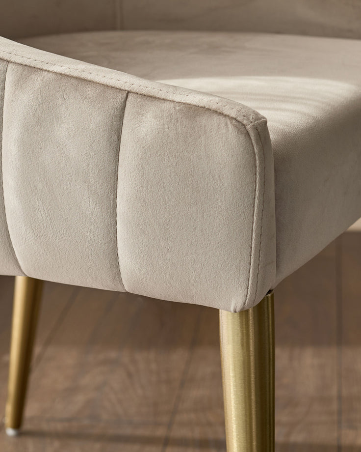 Champagne velvet dining chair with pleated seat detail and brushed brass legs, close-up side view.