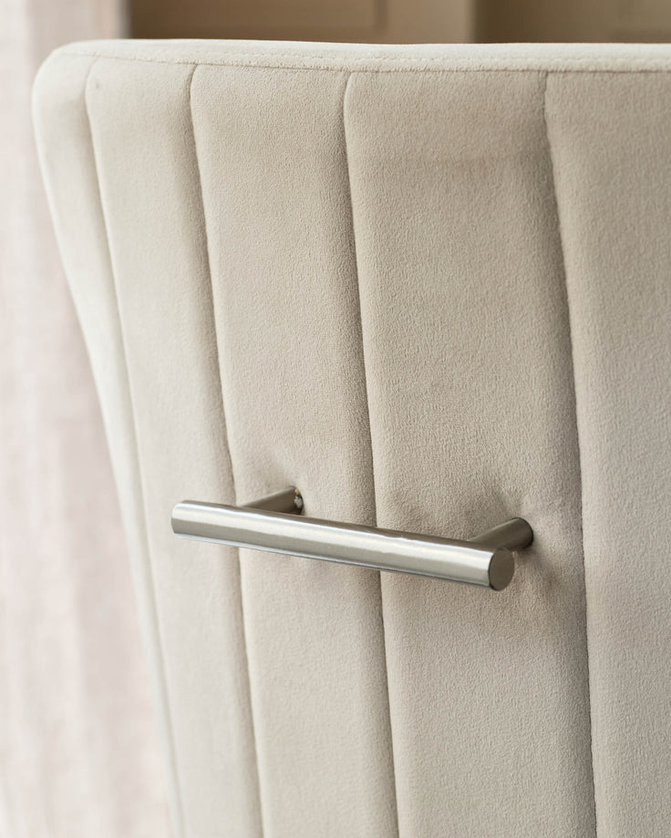 Champagne velvet dining chair with vertical channel stitching and brushed stainless steel handle detail.