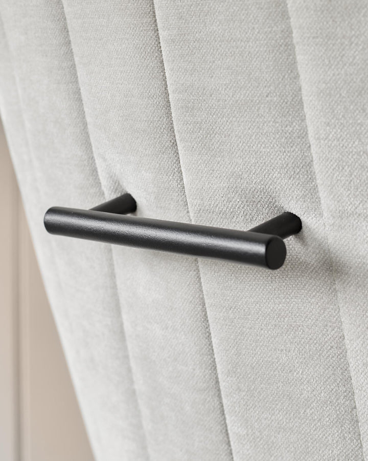 Close-up of a grey fabric chair with a black metal grab handle attached to the top of the seat back. Modern furniture design.