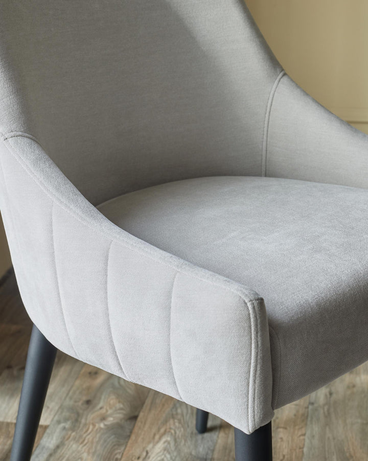 Close up of a light grey upholstered chair with dark legs on a wooden floor.