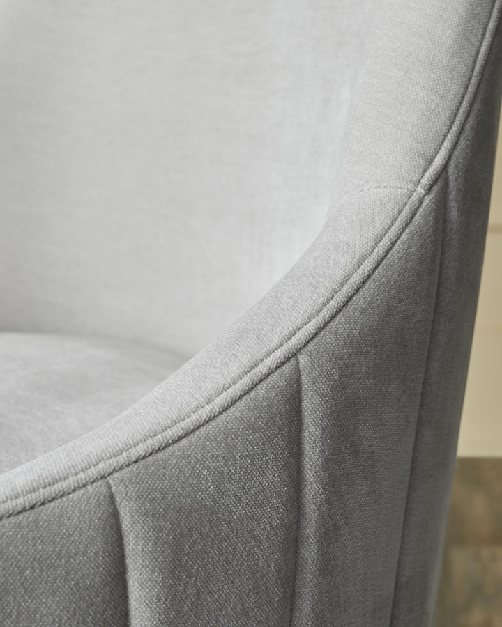 Close-up of a grey upholstered chair, showing the fabric's texture and the chair's curved design.