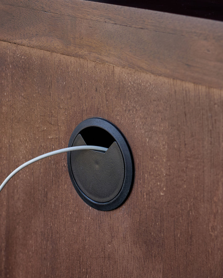 Dark mango wood bedside table with black oval cable management hole and white cord.