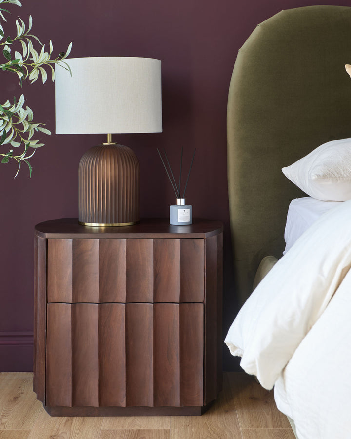 Dark mango wood bedside table with vertical panel detailing and two drawers, styled in a bedroom setting.