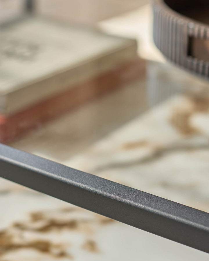 Close-up of a table with a grey metal frame and marble-look top. A tray and book are visible on the surface.