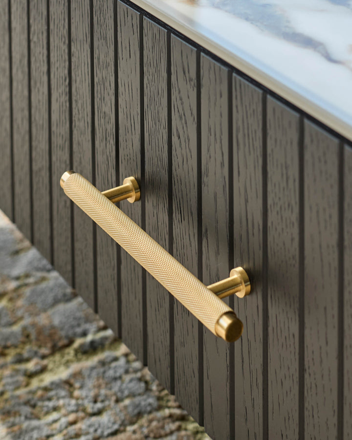 Close-up of a stylish, dark wood cabinet with a textured gold handle. Marble top partially visible.
