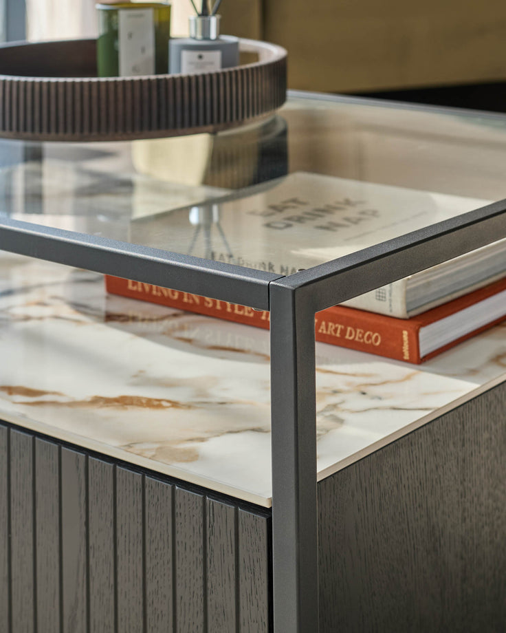 A sleek table with a glass top, supported by a dark grey frame and a faux marble shelf. Features stylish decor.