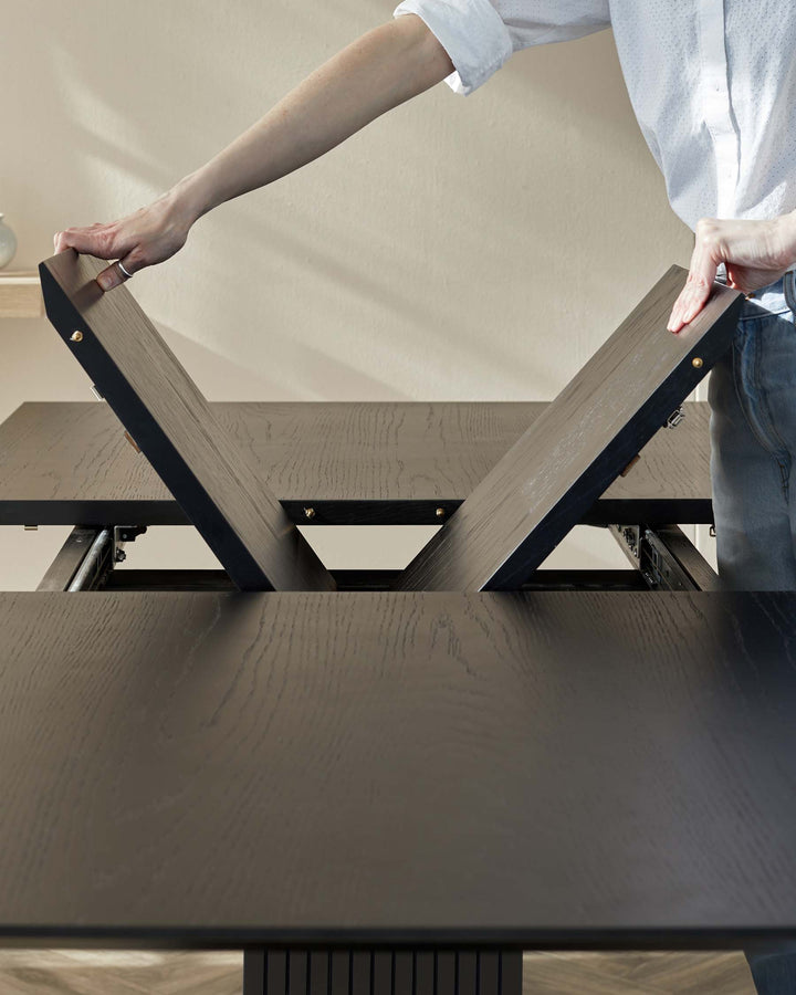 A dark wood extending dining table with a person adding leaves to the centre to make it larger.