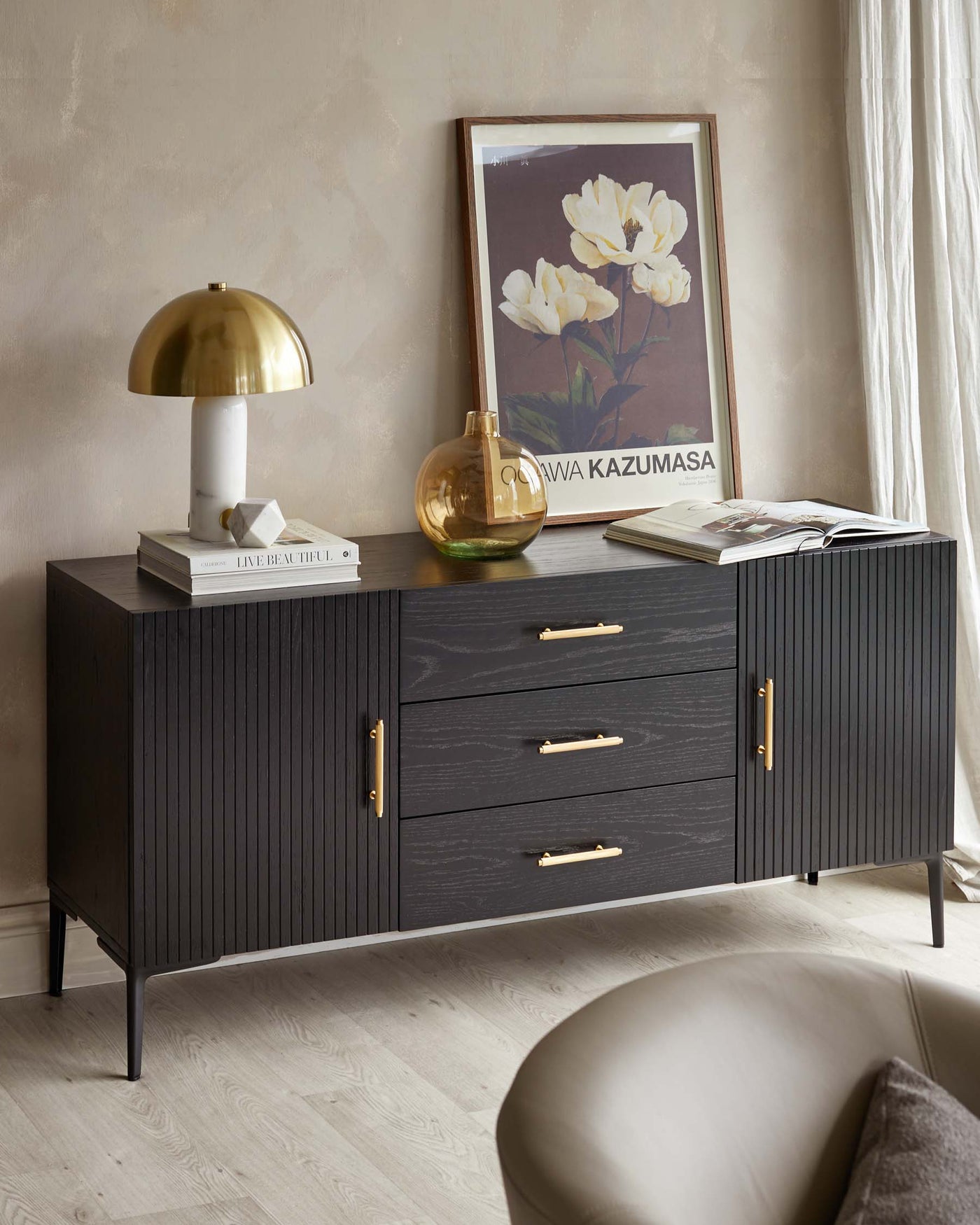 A contemporary dark wood sideboard with vertical fluted details and brass coloured handles. It stands on slender metal legs and showcases a symmetric design with two doors flanking three central drawers.