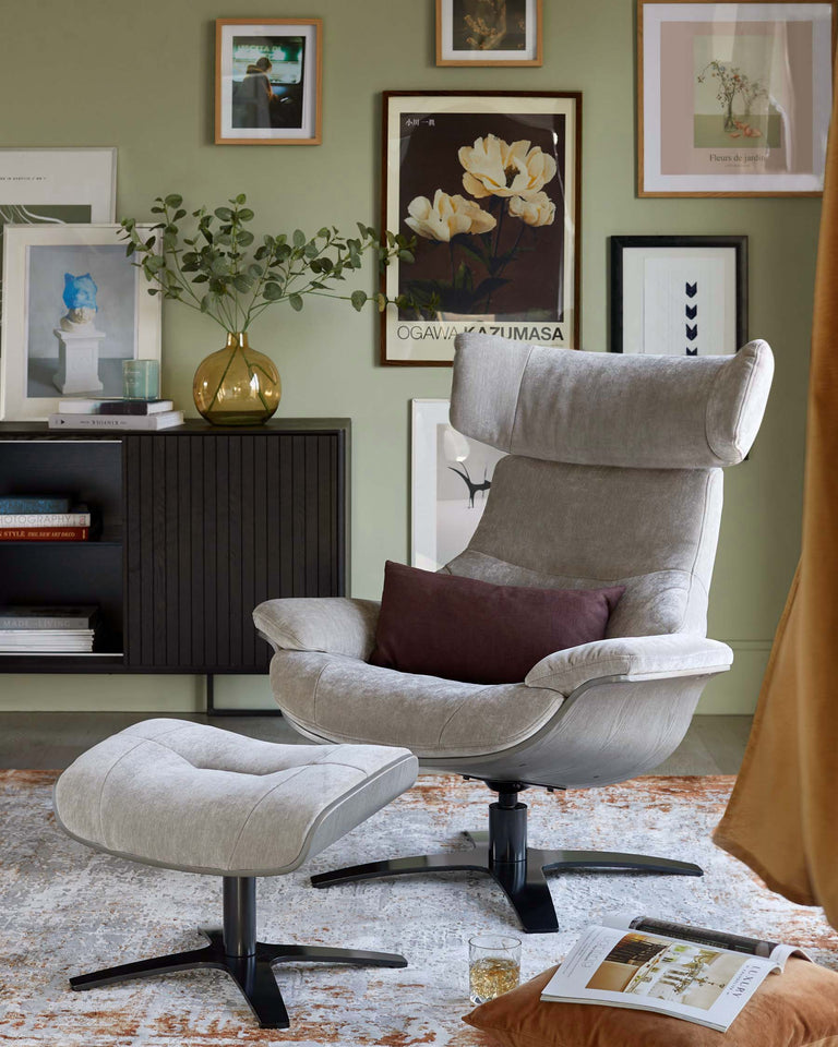 Modern grey upholstered swivel armchair with a matching footrest, featuring a tall contoured backrest, plush seating, and a dark star-shaped base. A minimalist black wooden sideboard with ribbed doors is partially visible in the background.