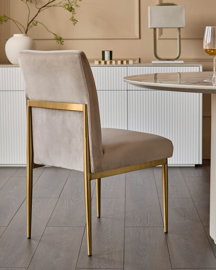 Keira velvet dining chair in champagne with gold metal legs, shown from a side angle in a modern dining room setting.