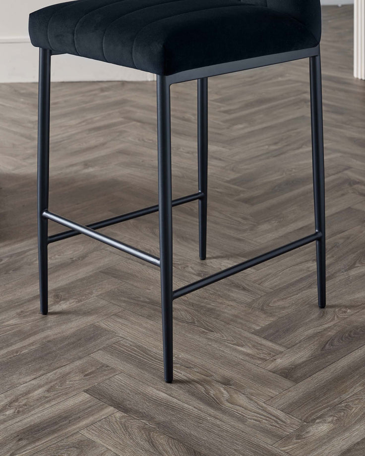 Modern black bar stool with a plush seat and a sturdy metal frame set against a wooden floor.