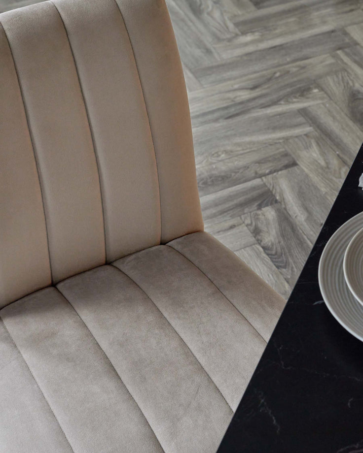 Elegant beige upholstered dining chair with pleated backrest, paired with a sleek black table and minimalist dishware.