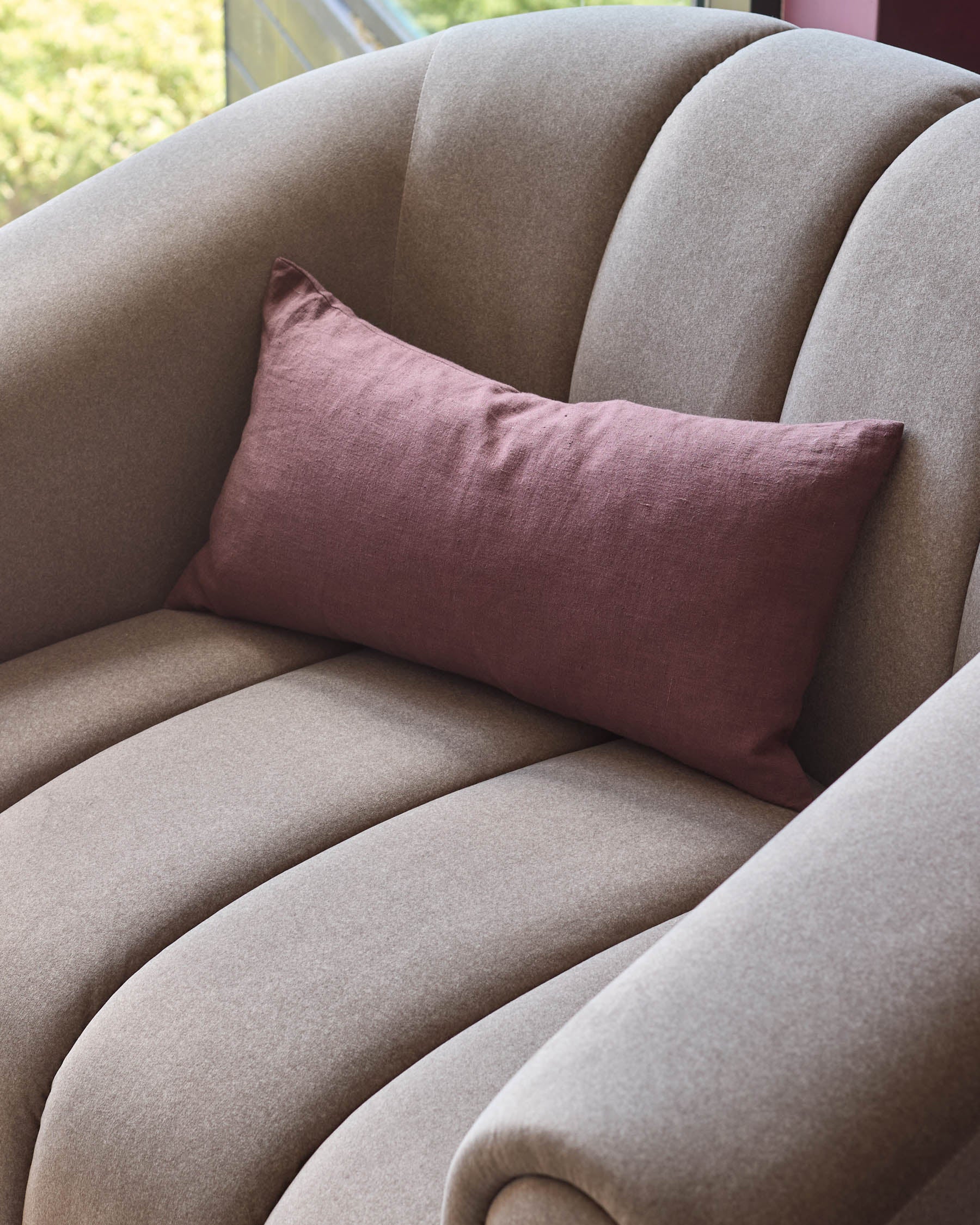 A close-up of a cosy, taupe armchair with a plush, pink rectangular cushion. Stylish and comfortable seating.