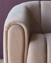 Close-up of a beige upholstered sofa with curved armrests against a purple wall, showcasing modern design and comfort.