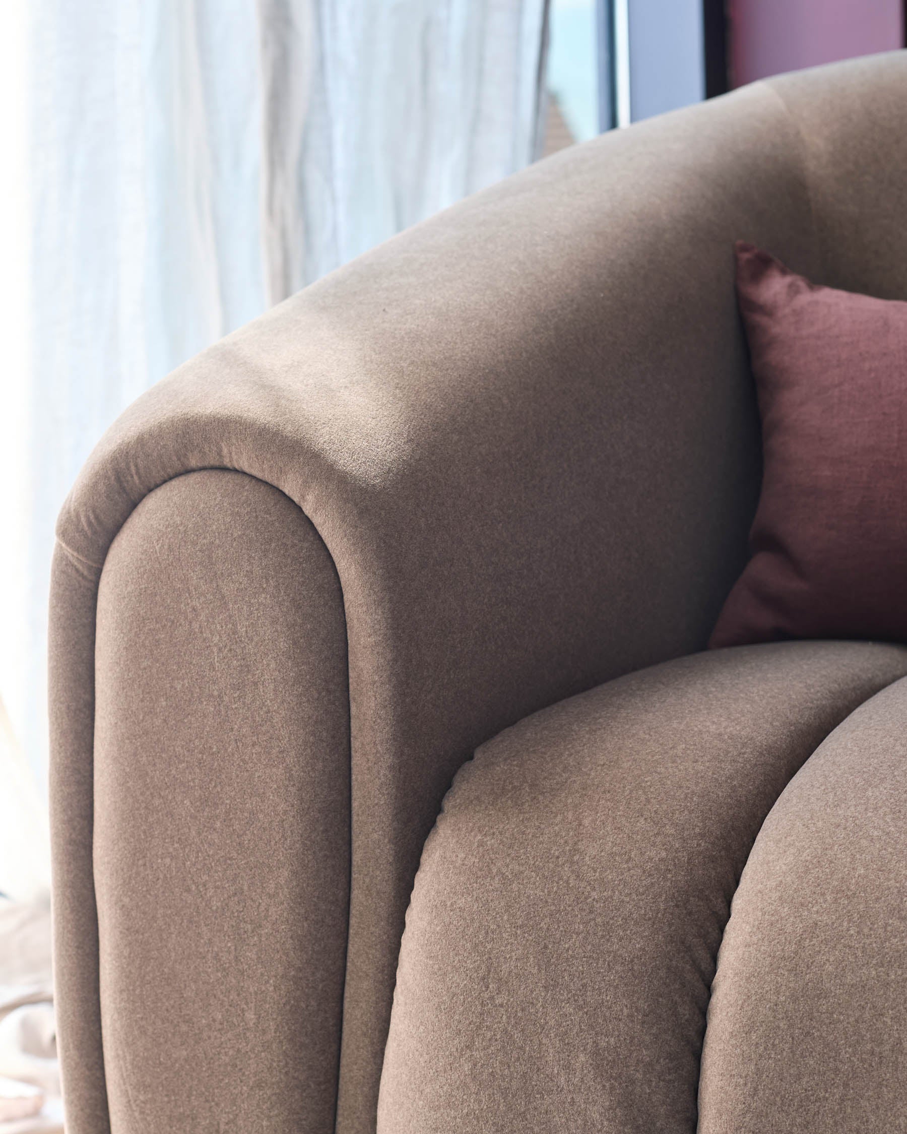 Close-up of a stylish, textured sofa with a plum cushion. Modern design with soft, neutral tones.