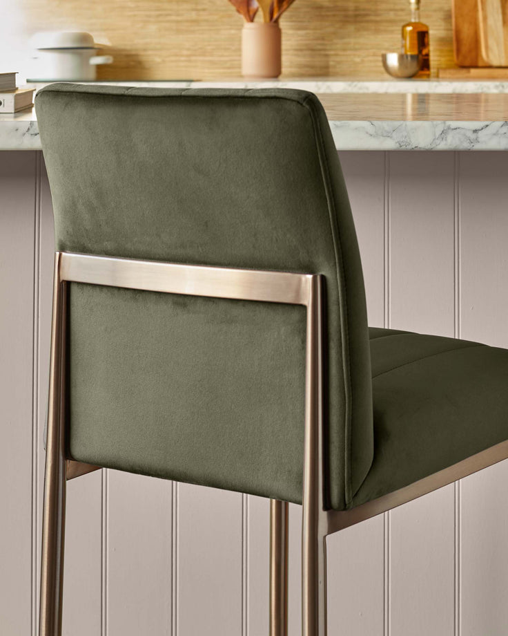Olive green velvet bar stool with bronze metal frame shown against a panelled wall.