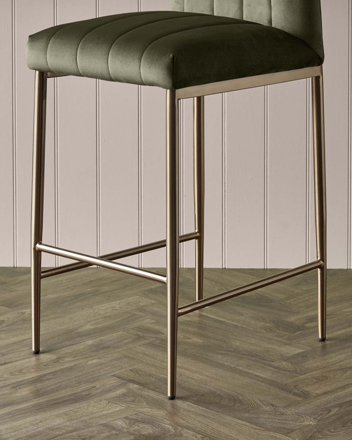 Close-up of a bar stool with an olive green seat and copper-coloured legs. The floor is herringbone wood.