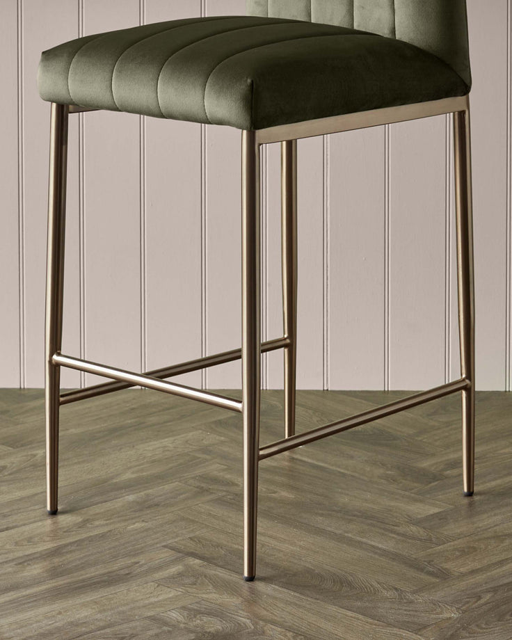 Close-up of a bar stool with an olive green seat and copper-coloured legs. The floor is herringbone wood.