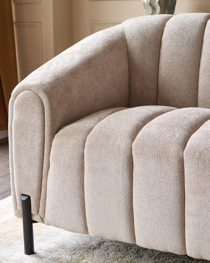 Kendra 3-seater sofa in natural fabric, showing curved channel-quilted design and rounded armrest from side angle.