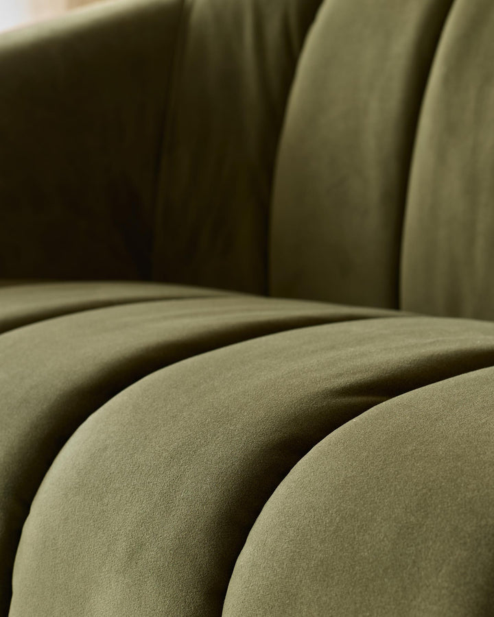 Close-up of an olive green velvet sofa showing the texture and form of the cushions.