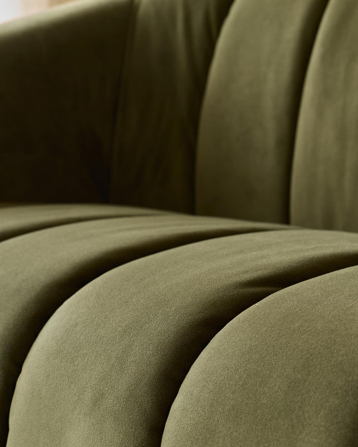 Close-up of an olive green velvet sofa showing the texture and form of the cushions.