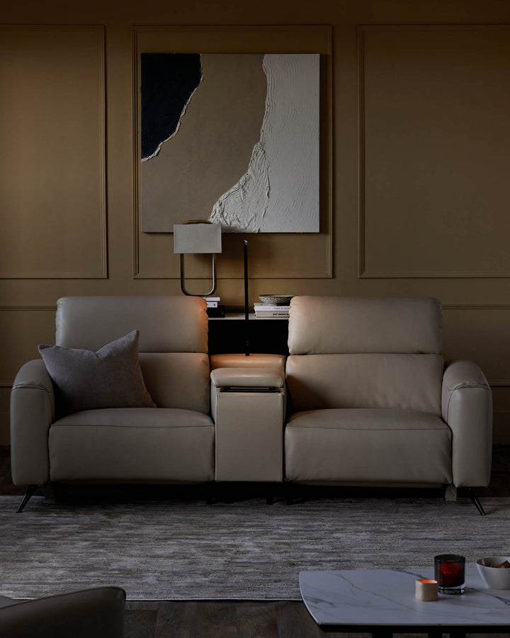 A cream leather two-seater sofa with built in console and a grey scatter cushion, placed on a patterned grey rug.