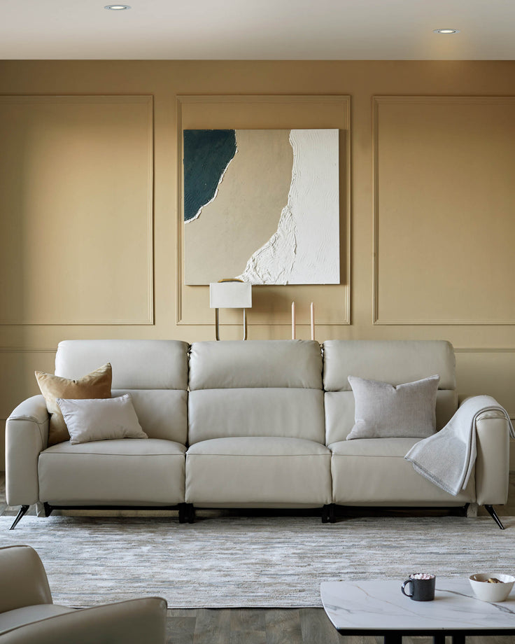 A stylish beige leather sofa adorned with cushions. Abstract art hangs above, complemented by a neutral colour scheme.