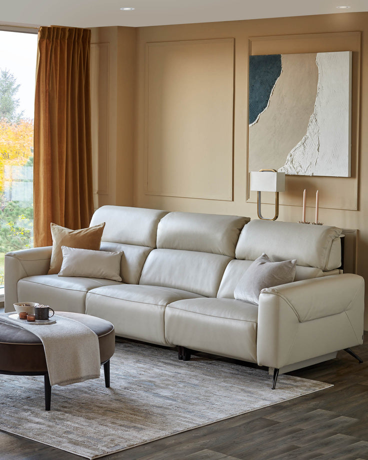 A modern, beige three-seater sofa with complementary cushions, an ottoman and a lamp, creating an inviting living space.