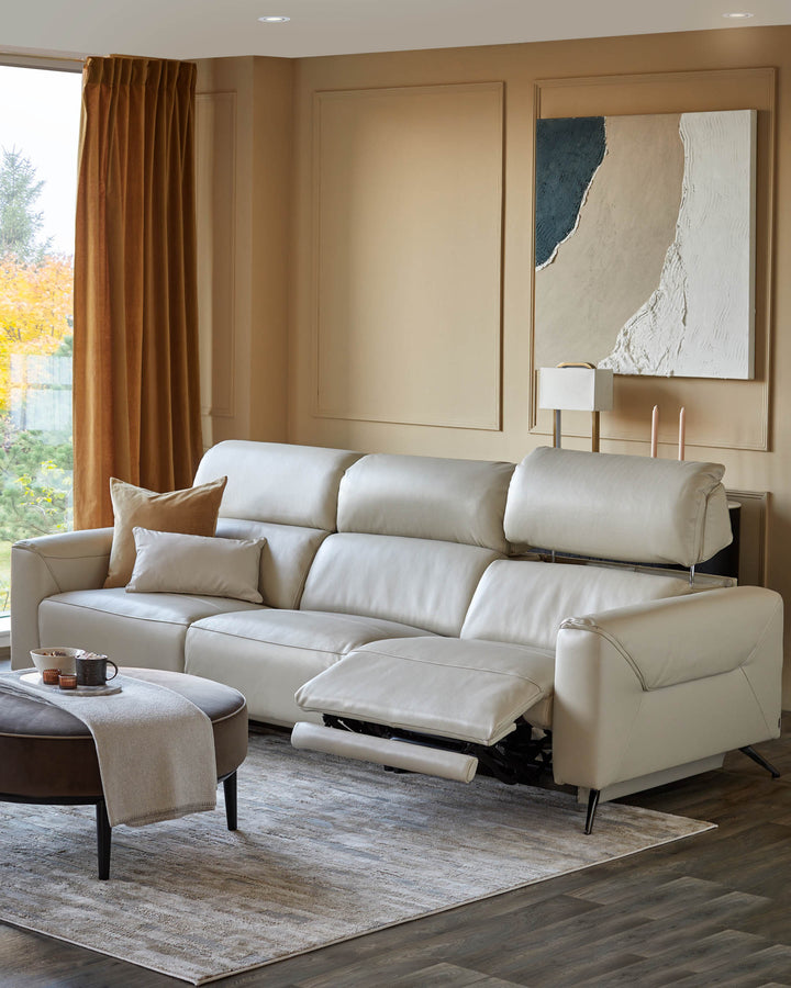 A modern living room featuring a cream leather sofa with recliner, matching ottoman and abstract art.