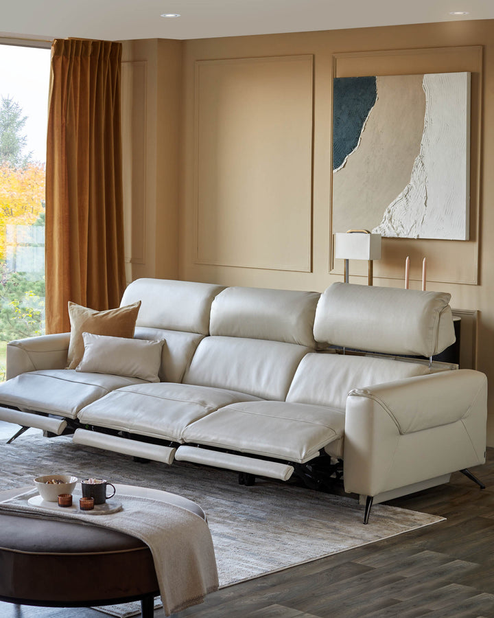 A sleek, cream-coloured leather sofa with reclining features, complemented by a stylish ottoman and modern artwork.