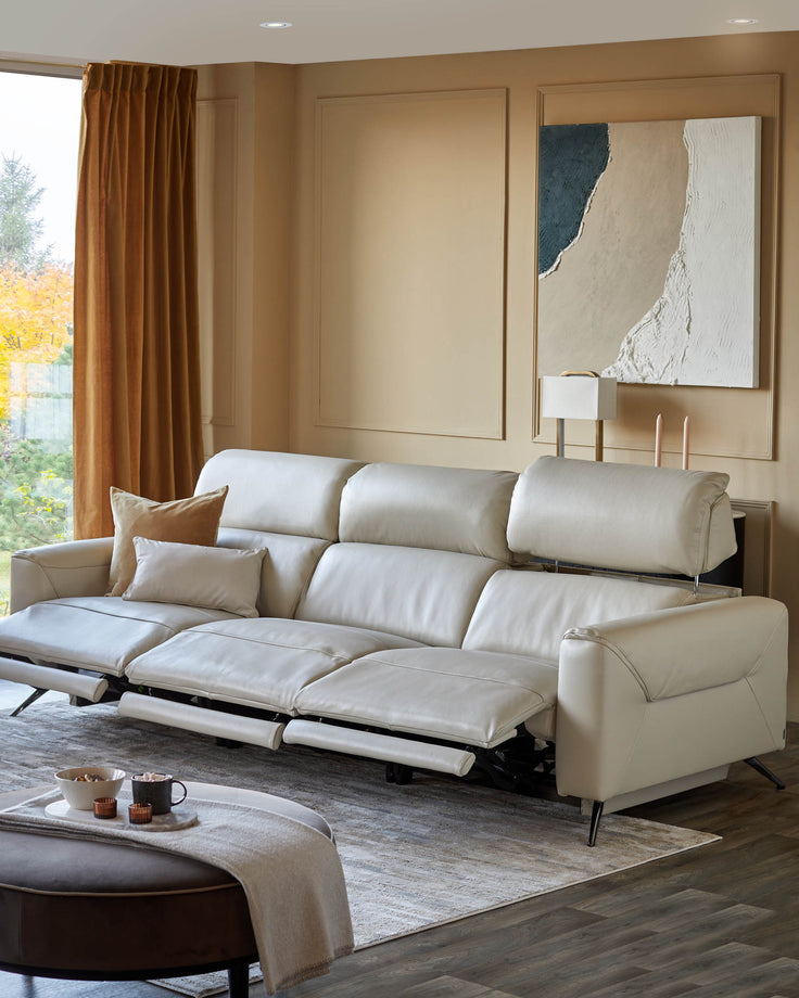 A sleek, cream-coloured leather sofa with reclining features, complemented by a stylish ottoman and modern artwork.