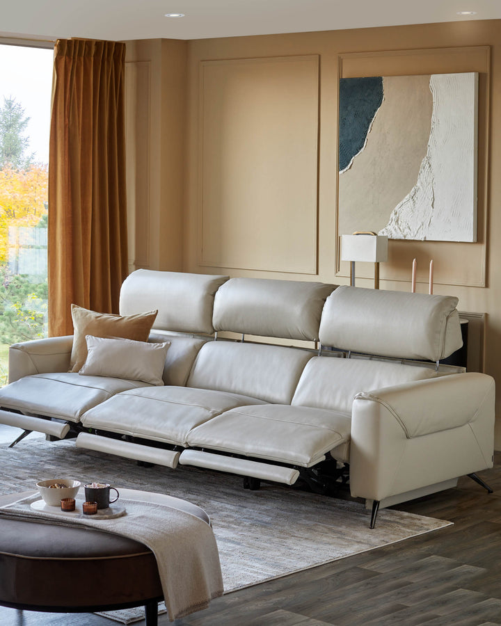 A luxurious beige leather sofa with reclining seats and adjustable headrests, complemented by a brown ottoman.