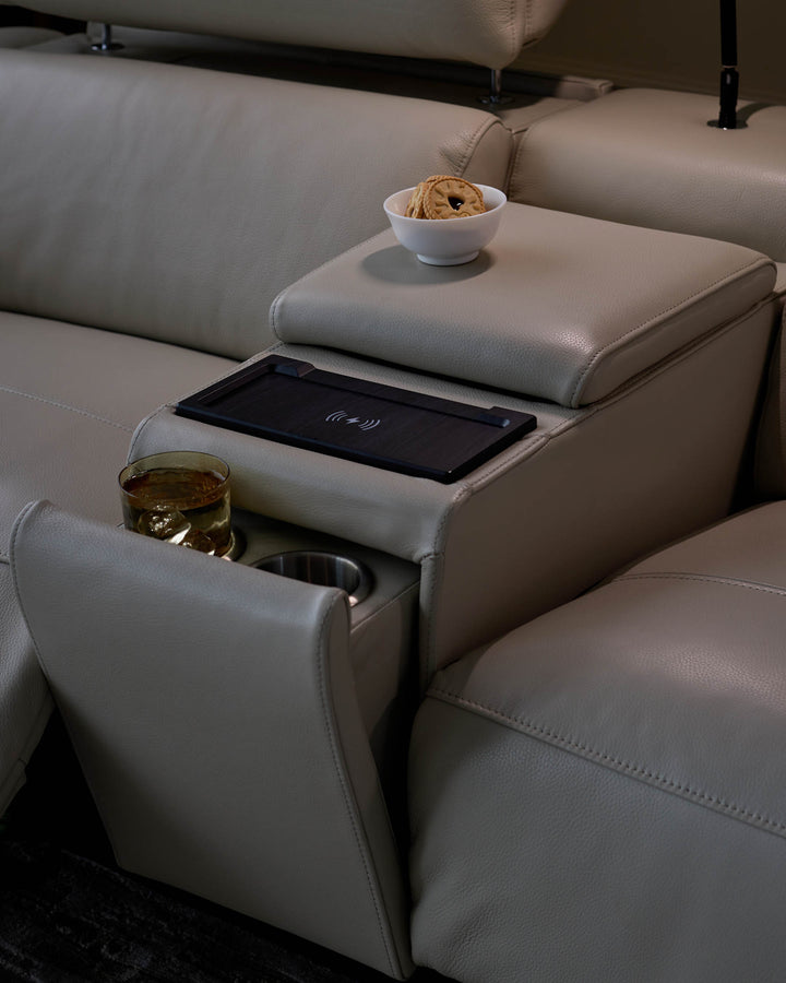 A stylish light-grey leather reclining sofa features a wireless charging pad and cup holders.