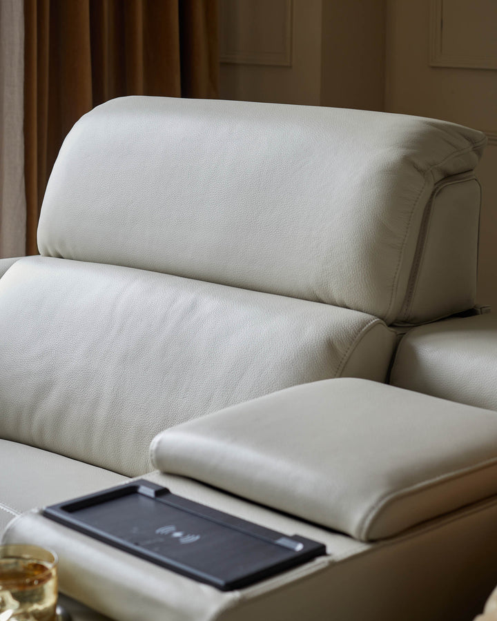 Close-up of a modern white leather sofa with adjustable headrests and a built-in wireless charging pad.