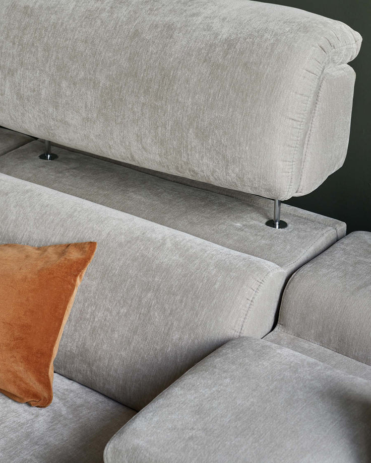 Modern grey velvet sectional sofa with a plush design, featuring sleek metal legs and a contrasting orange throw pillow.