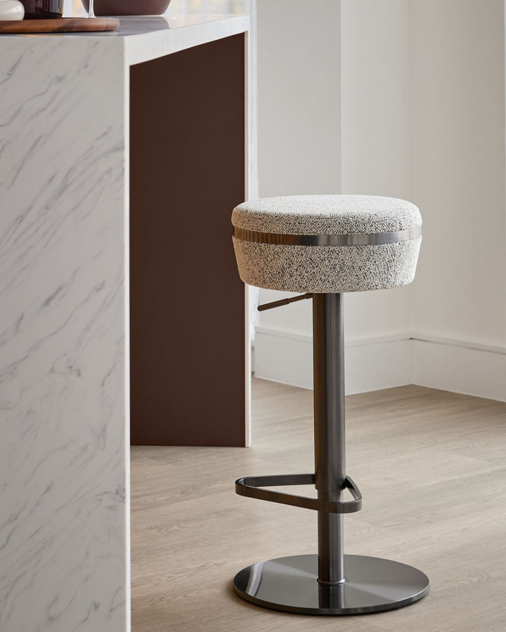 Kian gas lift bar stool in grey fabric with dark bronze metal base and footrest, shown in modern kitchen setting.
